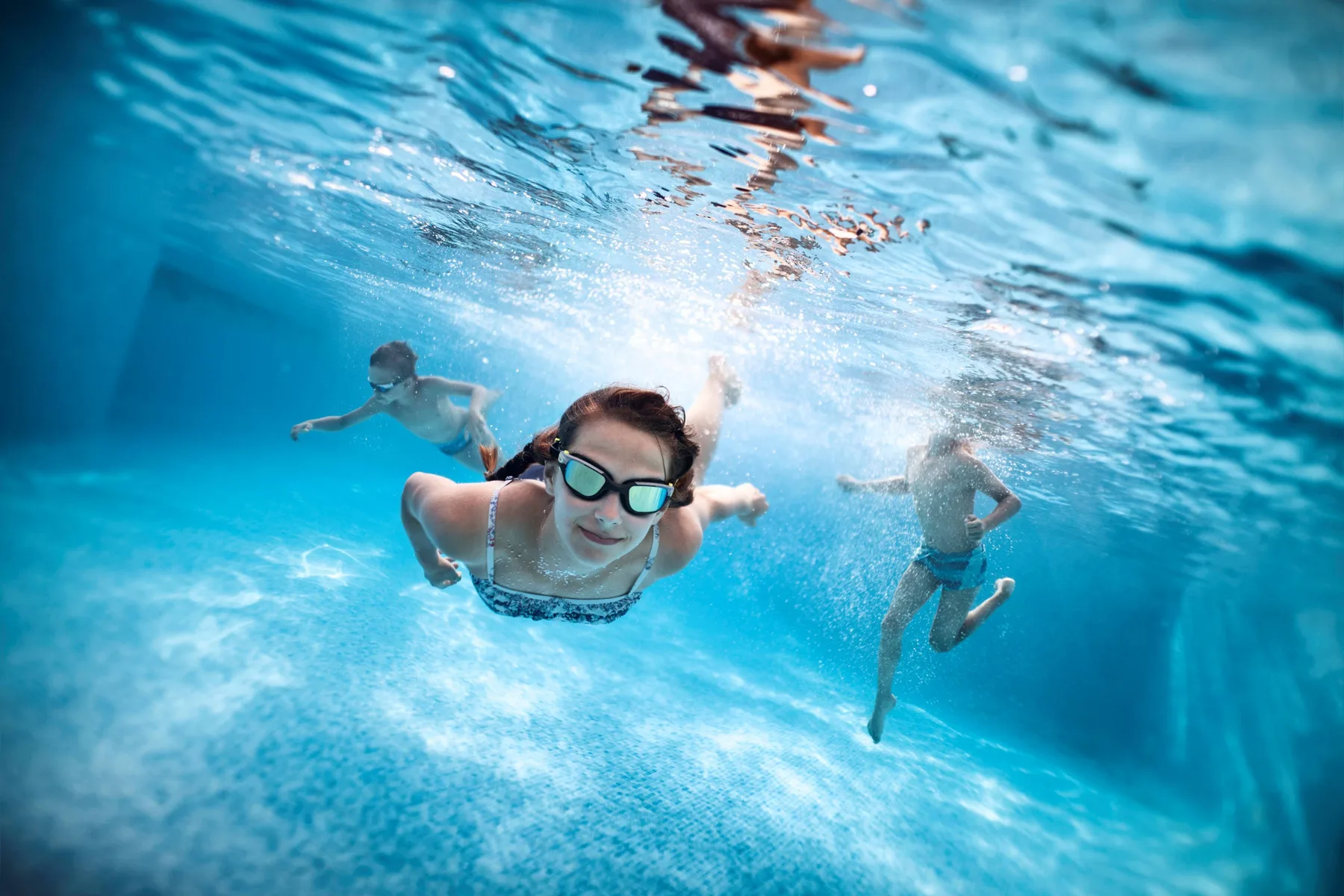 Kids swimming underwater in a clear blue pool