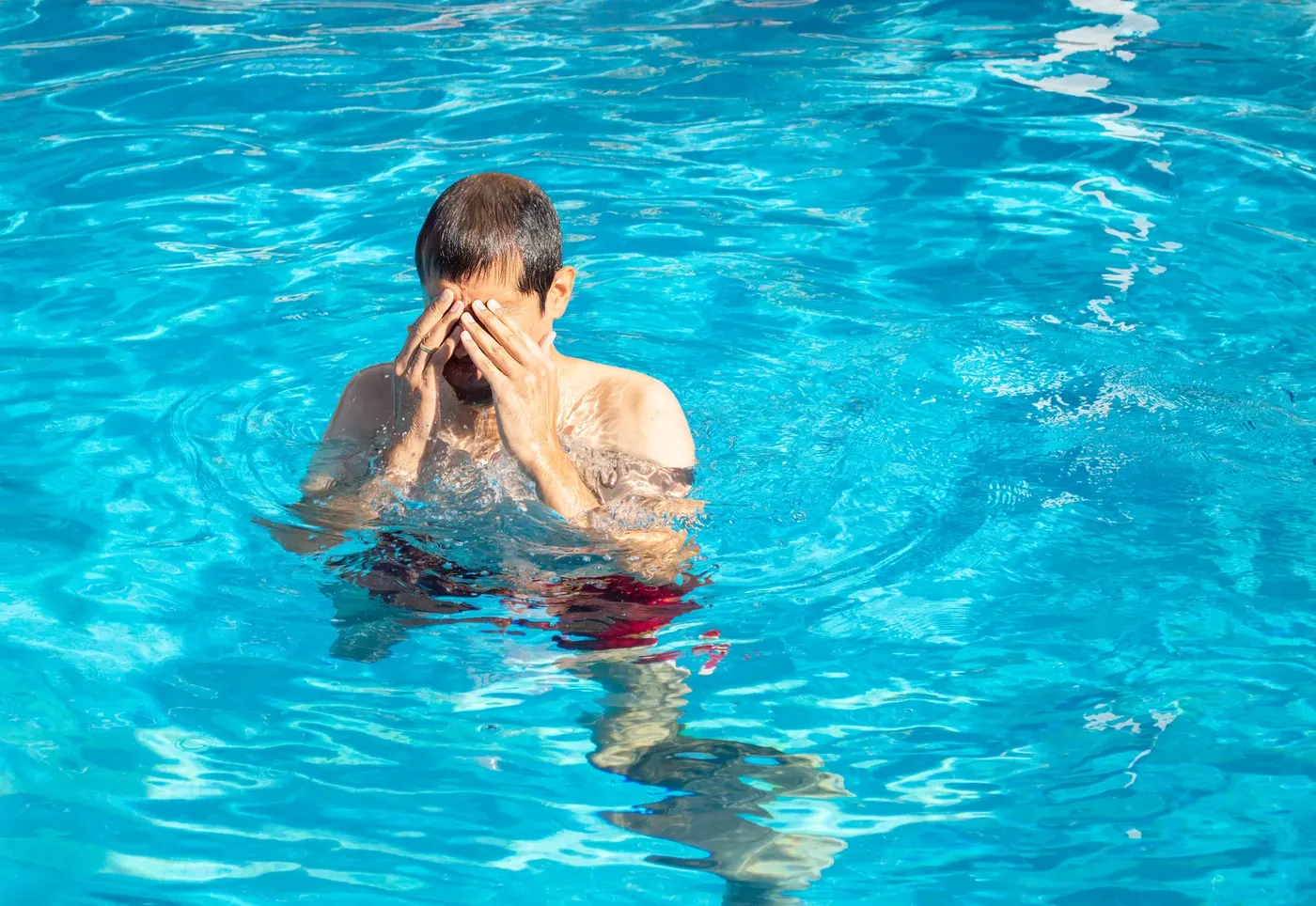 A swimmer standing in a pool, rubbing stinging eyes