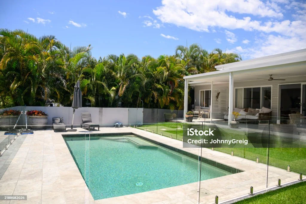 A sunny backyard pool behind a glass fence