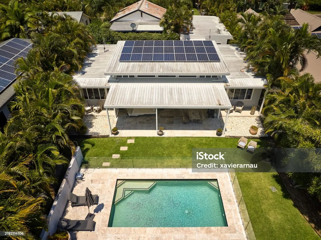 Aerial view of a house with rooftop solar panels and a fenced backyard pool