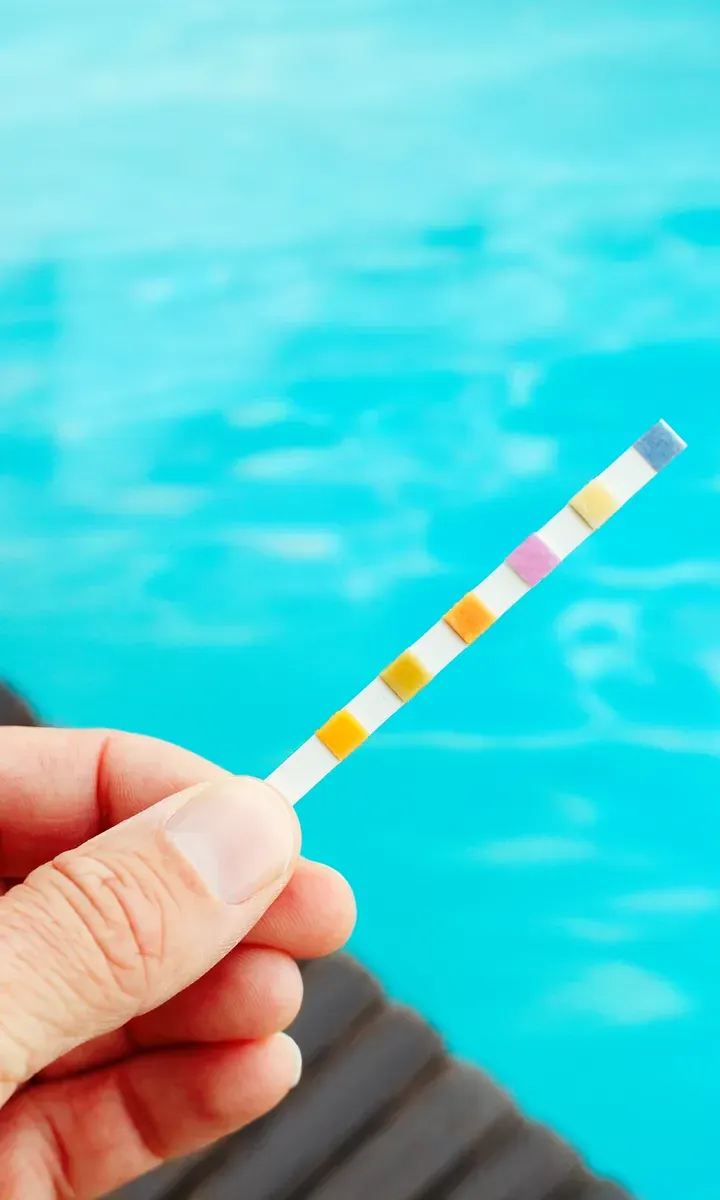 A pool test strip held up against clear blue water